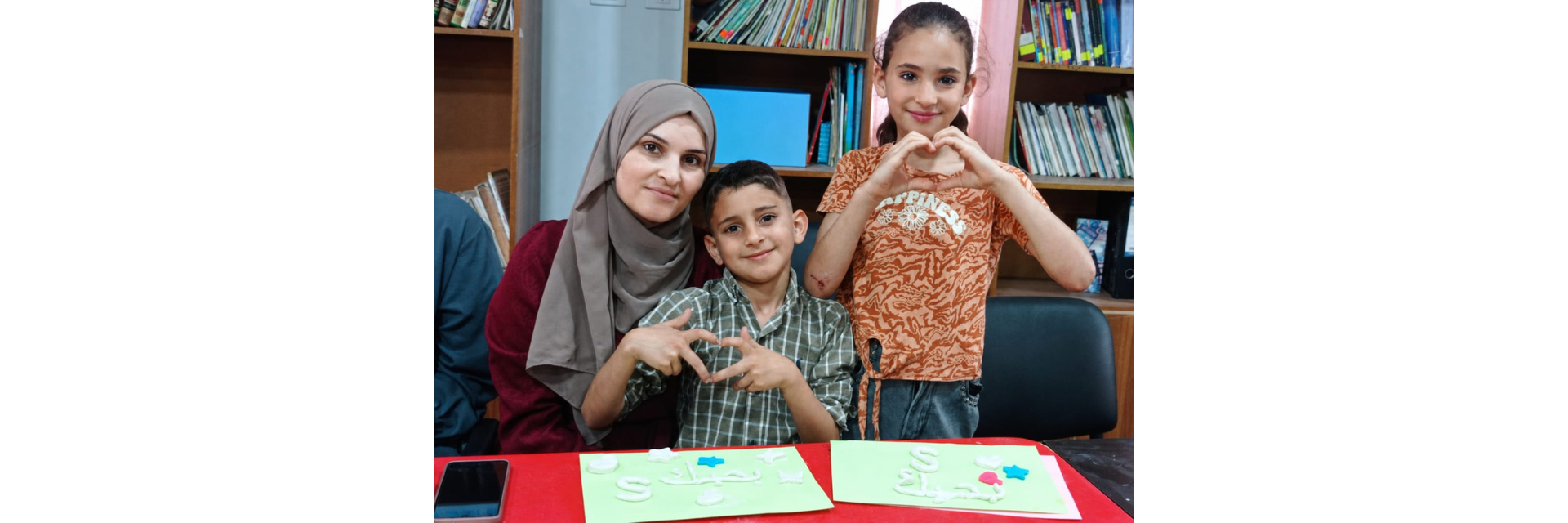 Une mère et ses deux enfants forment des cœurs avec leurs mains tout en créant des cartes faites à la main au club Makani.