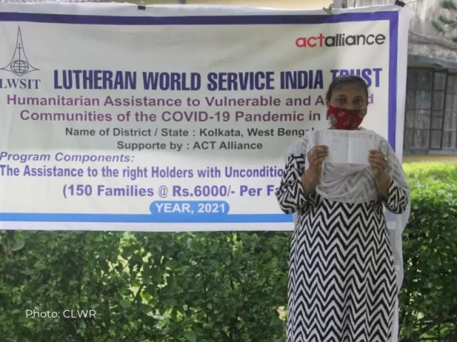 Shila Mondal debout devant une affiche du programme avec son document de transfert d'argent