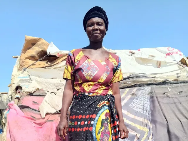 A woman in colourful clothing stands in front of a shelter