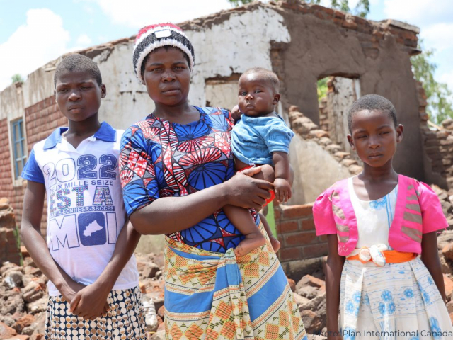 Femme avec ses enfants devant leur maison endommagée