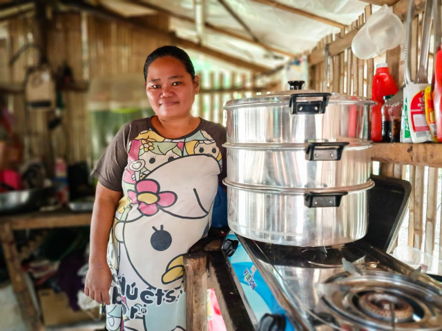 Une femme se tient dans une cuisine, à côté d'un ensemble de grands paniers à vapeur posés sur la cuisinière.