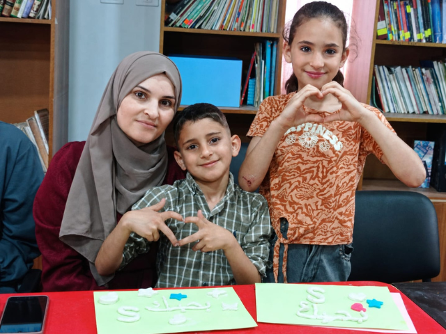 Une mère et ses deux enfants forment des cœurs avec leurs mains tout en créant des cartes faites à la main au club Makani.