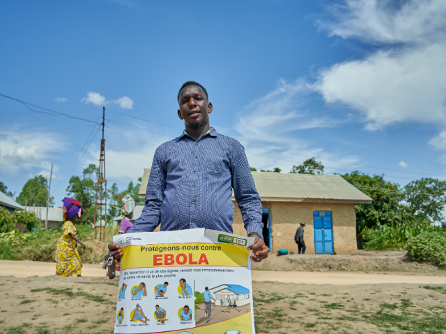 Un homme tenant une affiche sur laquelle il est écrit : « Protégeons-nous contre Ebola ».