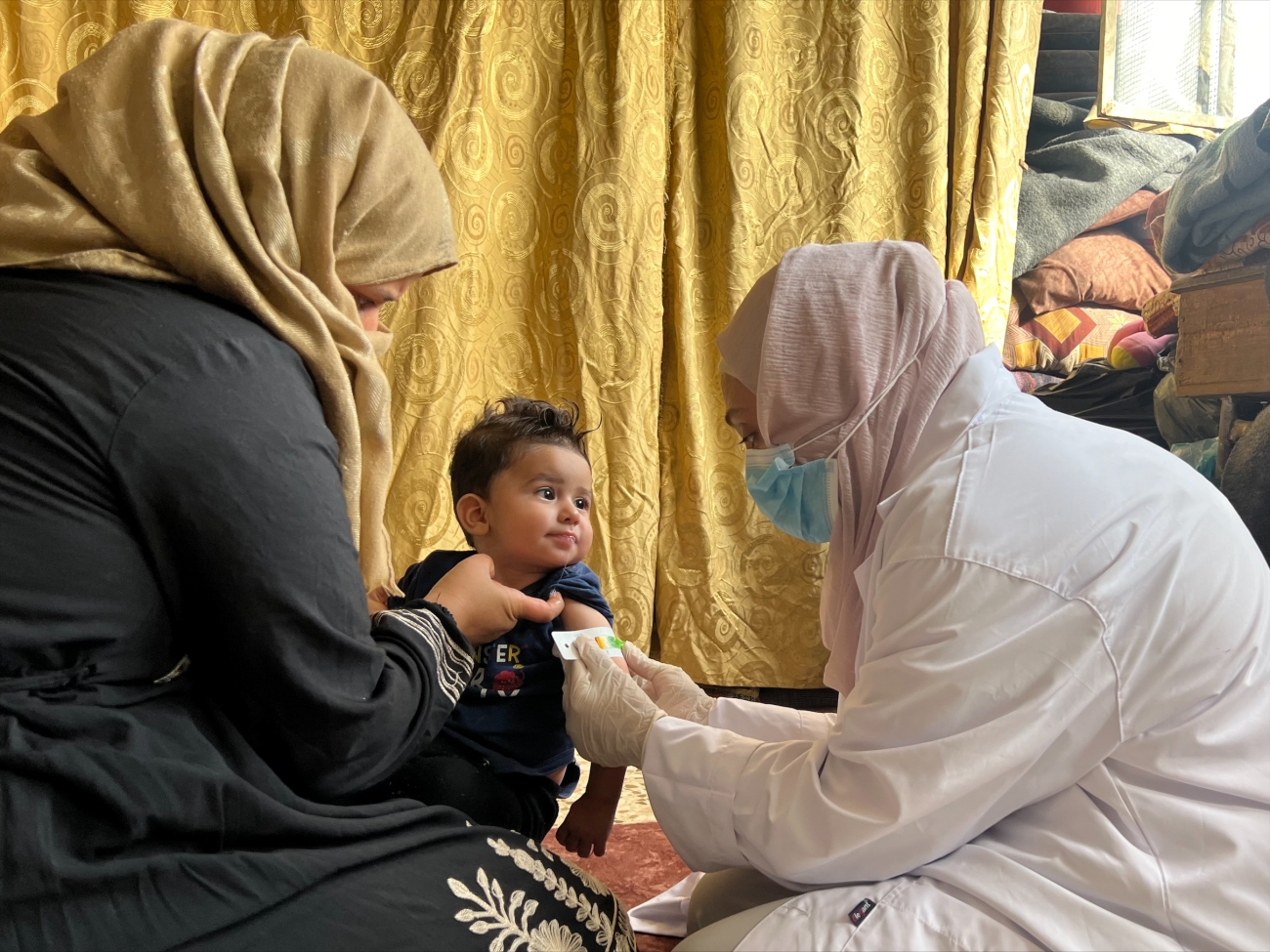 A caregiver comforts a child as a healthcare worker checks for signs of malnutrition
