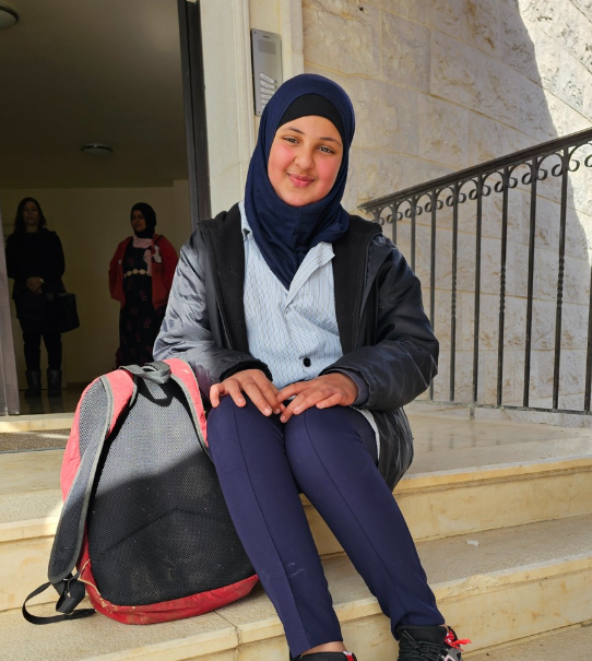 Lana on the steps of the education centre, with her mother Fatouma standing behind her.
